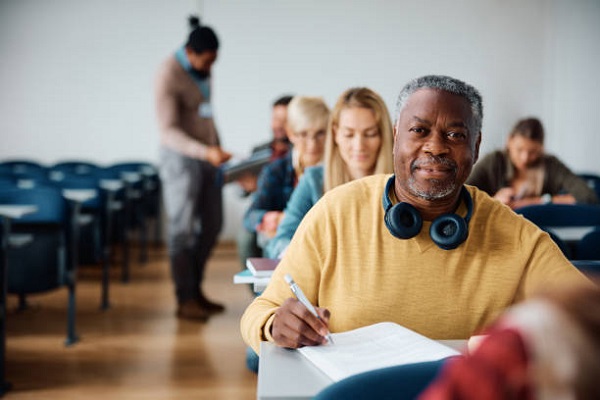 advanced Smiling African American senior man writing educational exam in the classroom and looking at camera.