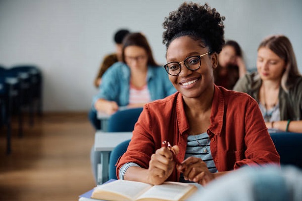 intermediate Happy African American woman attending a lecture in university classroom and looking at camera.